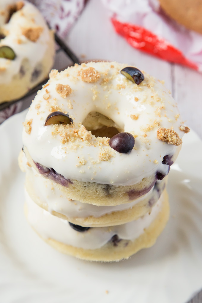 These Baked Blueberry Cheesecake Doughnuts are filled with juicy blueberries and topped with the most amazing cream cheese frosting and biscuit crumbs.