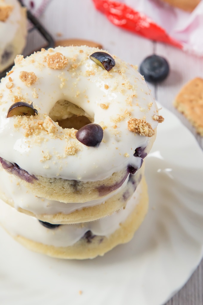 These Baked Blueberry Cheesecake Doughnuts are filled with juicy blueberries and topped with the most amazing cream cheese frosting and biscuit crumbs.